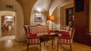 Un hall d’hôtel avec un plancher en bois, des canapés à rayures et des fauteuils. On y trouve une cheminée, un tableau encadré au mur et une porte avec une fenêtre.