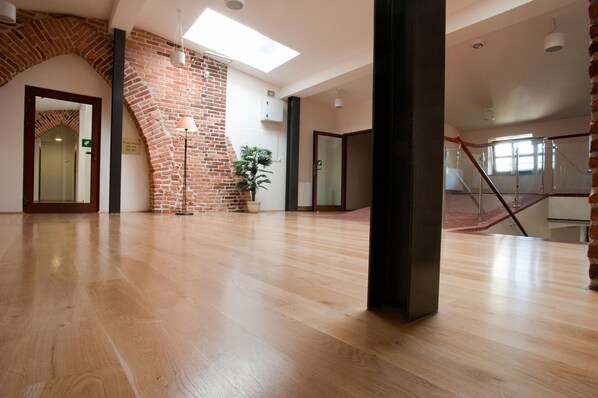 A spacious room with a wooden floor, a brick wall, and a skylight.