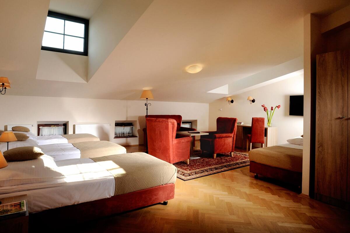 Una habitación de hotel moderna con una cama grande, un escritorio, dos sillas rojas, una mesita pequeña y un televisor en la pared.