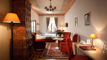 Habitación de hotel con cama, escritorio con lámpara, silla, sillón rojo, armario de madera y candelabro.