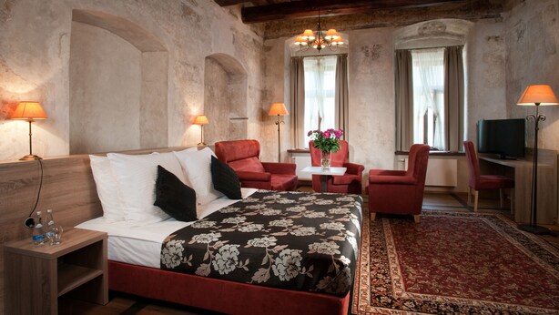 Une chambre à coucher avec un lit, deux fauteuils rouges, une petite table avec un vase et un téléviseur.