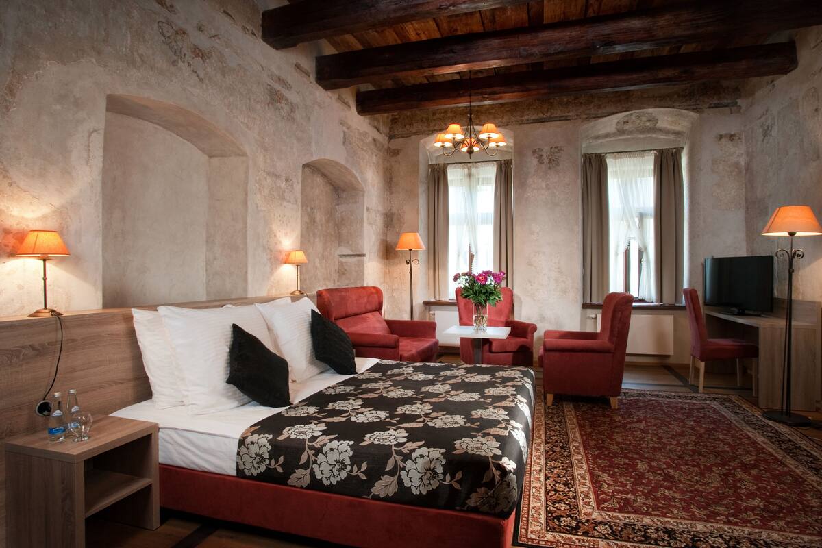 Un dormitorio con una cama, dos sillones rojos, una mesita con un jarrón y una televisión.