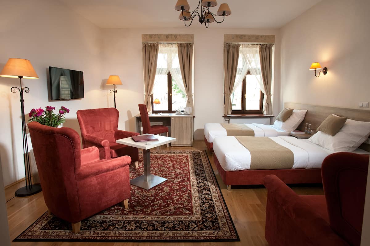 Habitación de hotel con sofá rojo, una mesita, cama con dos almohadas, mesita de noche y lámpara.