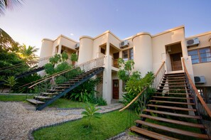 A multi-story hotel with external staircases, air conditioning units, and a well-maintained garden area. - Casa Rex by Sol Resorts (Vilanculos)