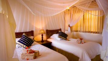 A hotel room with two beds, each with a pillow and a rolled towel. There is a nightstand with a lamp between the beds.