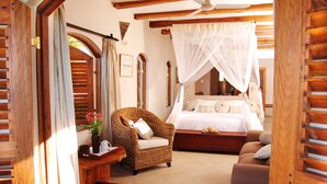 A bedroom with a canopy bed, a wicker armchair, a wooden bench, and a view of the outdoors through an arched doorway. - Casa Rex by Sol Resorts (Vilanculos)