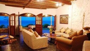 A cozy lounge area with a stone floor, two sofas with cushions, a coffee table, and a view of the sea through open doors. - Casa Rex by Sol Resorts (Vilanculos)