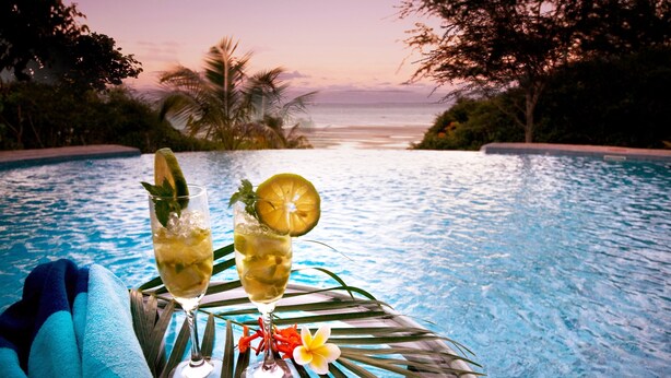 A poolside view with two glasses of a beverage, a tropical setting, and a view of the ocean. - Casa Rex by Sol Resorts (Vilanculos)