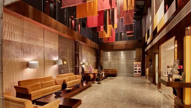 Een ruime lobby met een modern design, met een centraal zitgedeelte met banken en een salontafel, een receptiebalie en een grote spiegel.