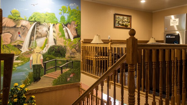 A hotel lobby with a mural of a waterfall, a wooden staircase, and a refrigerator with an ice dispenser. - Red River Inn Silt-Rifle (Silt)