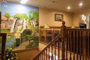 A hotel lobby with a mural of a waterfall, a wooden staircase, and a refrigerator with an ice dispenser. - Red River Inn Silt-Rifle (Silt)