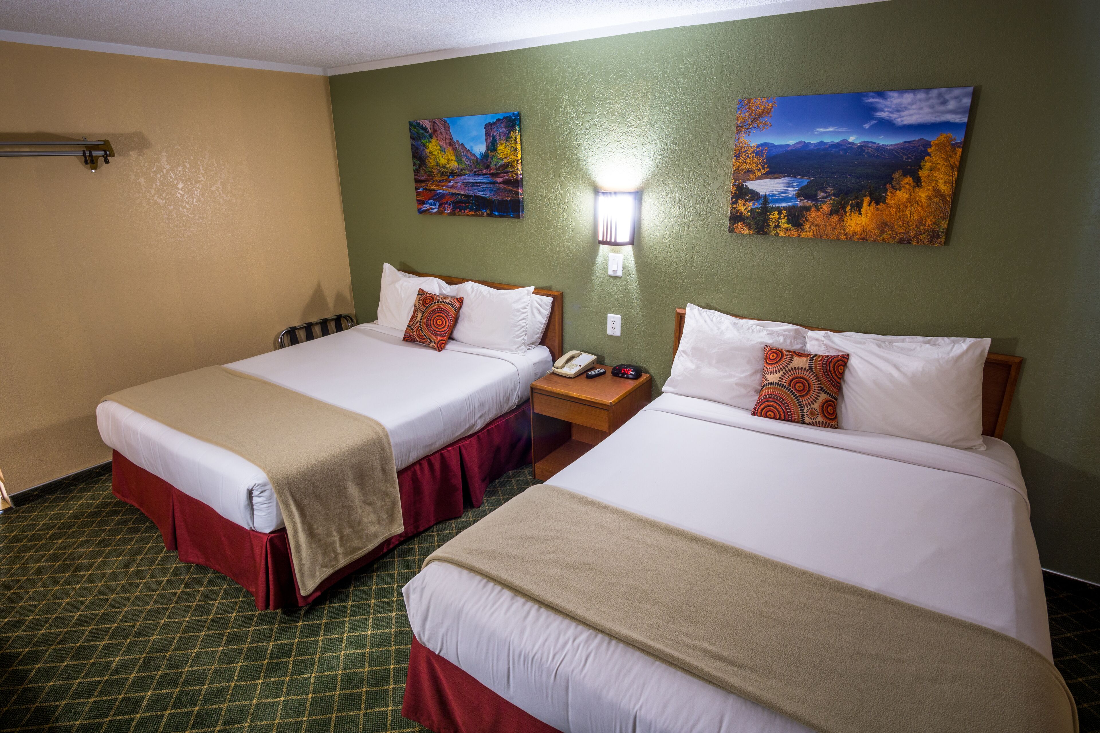 A hotel room with two beds, a nightstand, and two paintings on the wall.