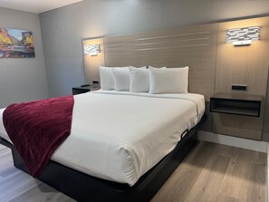 Ein modernes Hotelzimmer mit einem großen Bett, einer roten Tagesdecke, zwei Nachttischen und einer Wandleuchte.