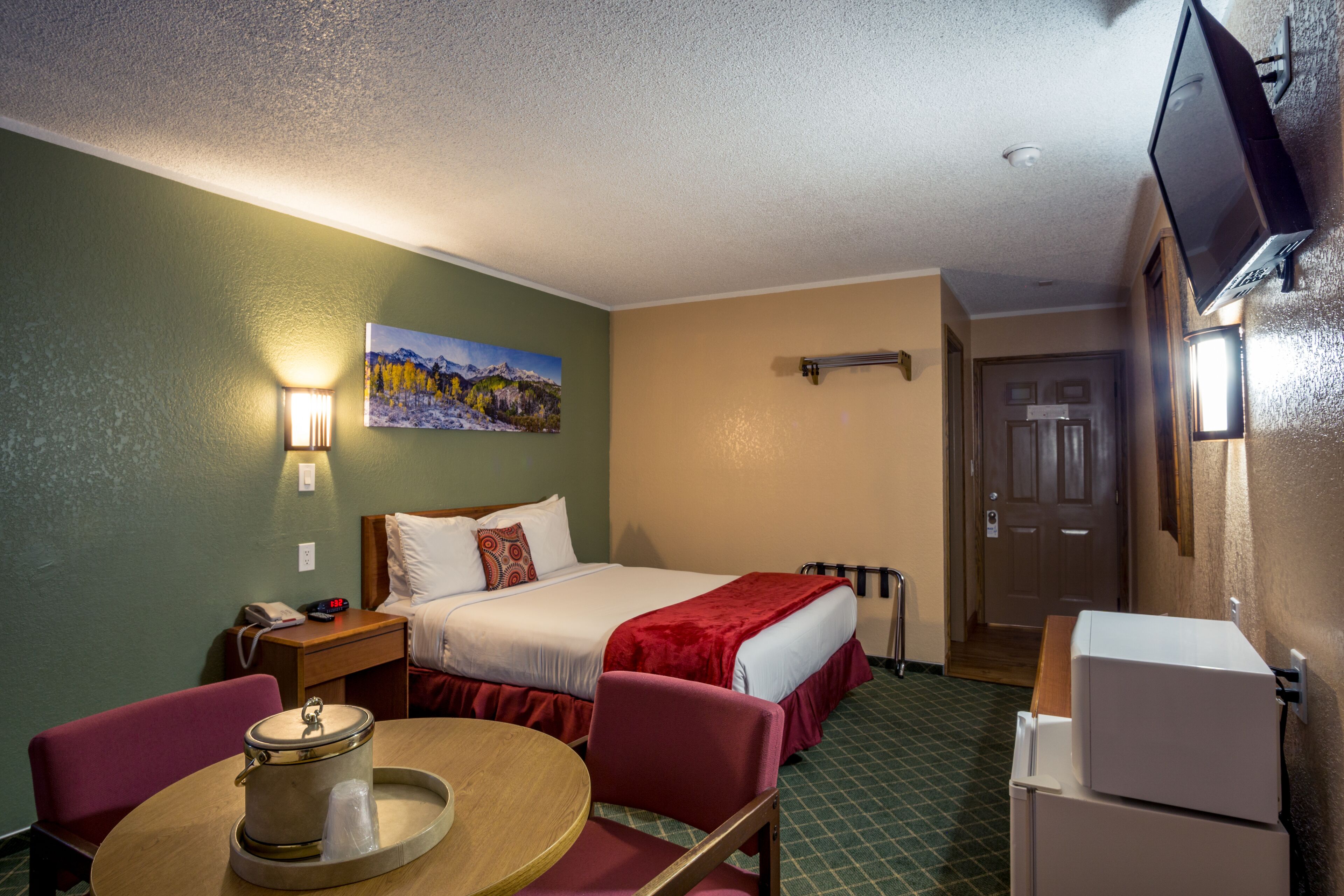 A hotel room with a bed, a desk with a lamp, a television, and a refrigerator.
