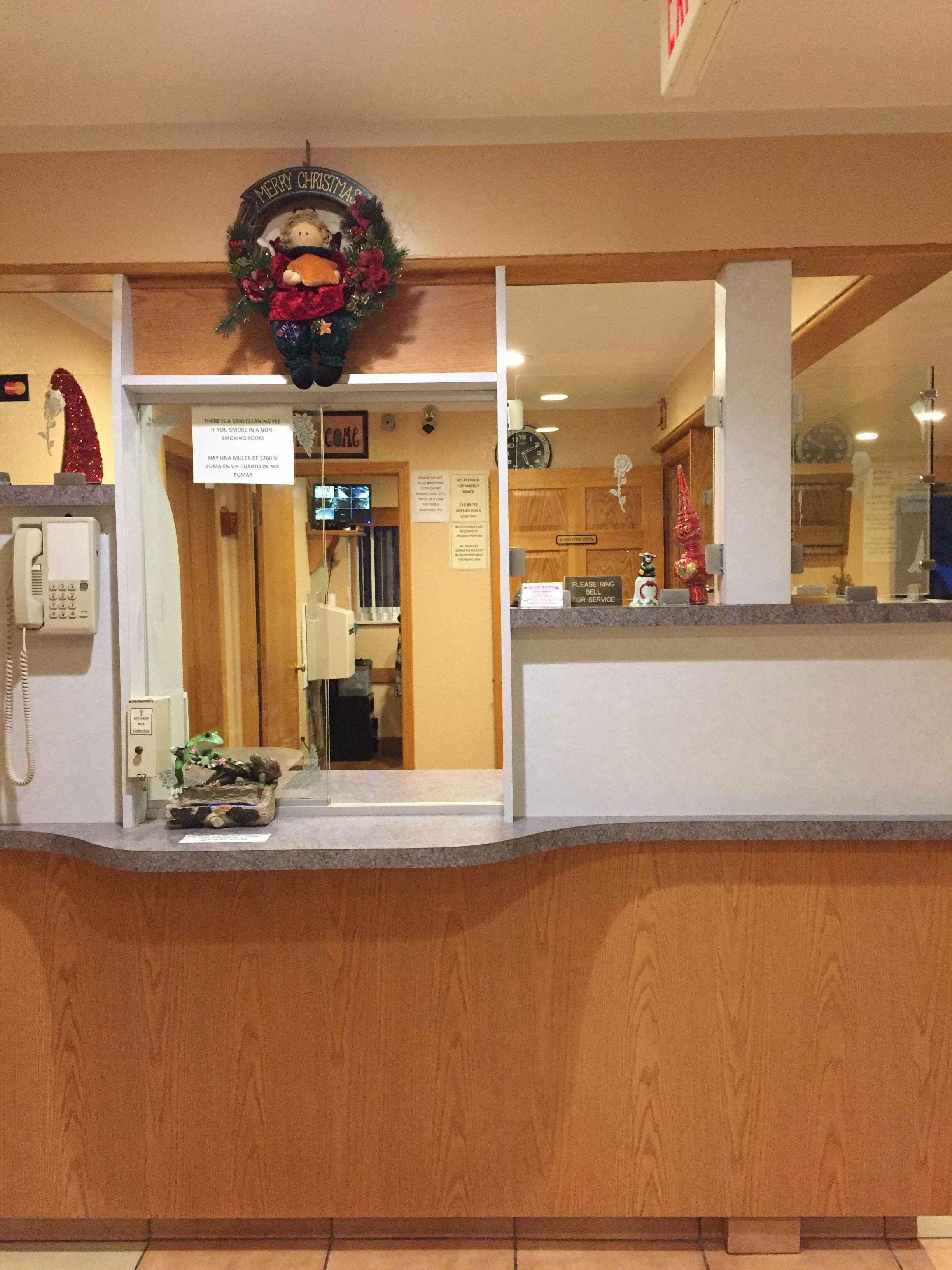 Et hotelreceptionsområde med en trædisk, et skilt med 'Merry Christmas', et 'Welcome'-skilt, et ur og et skilt, der siger 'Ring på klokken eller kontakt service'.