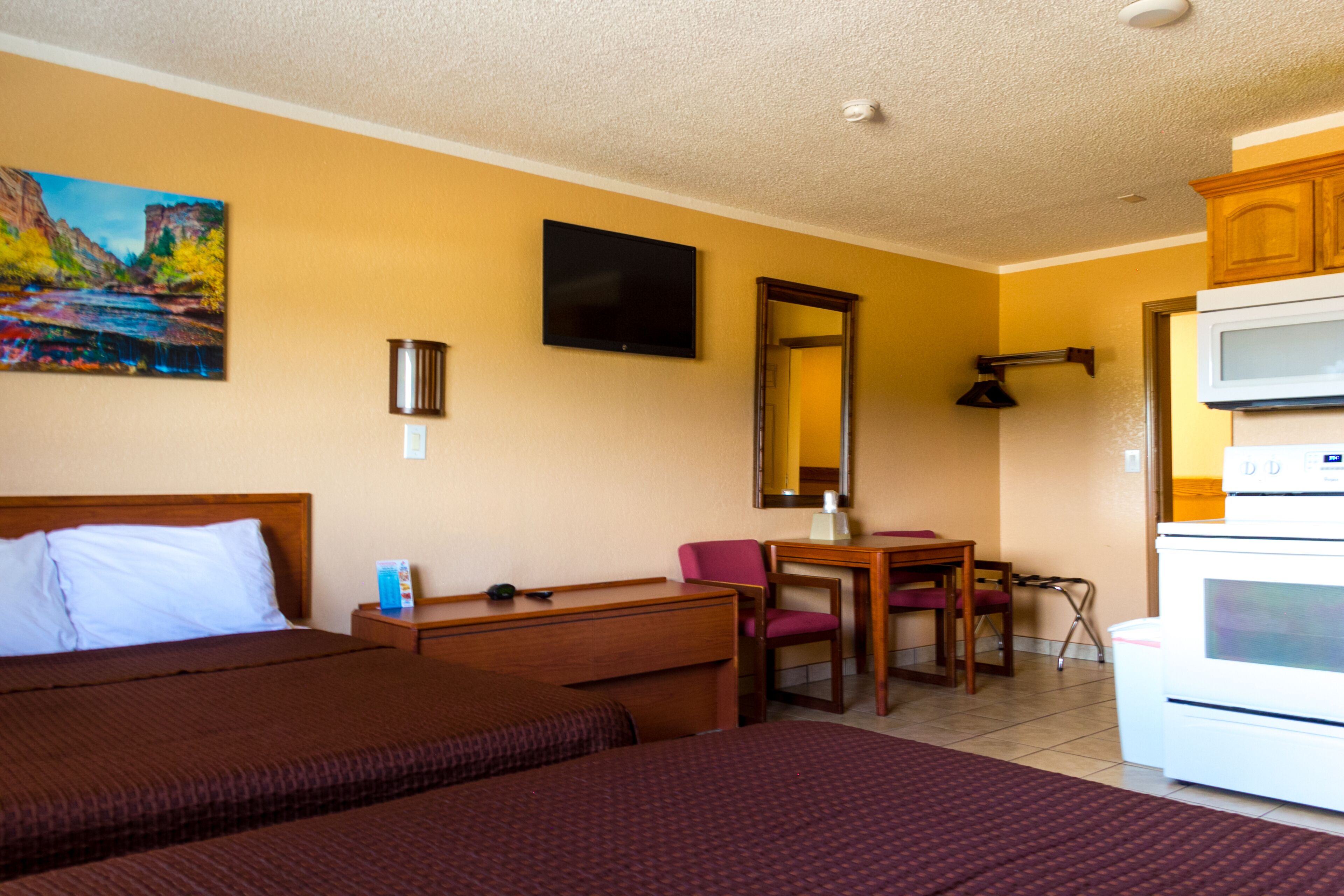 Habitación de hotel con dos camas, un escritorio, una silla, un televisor, microondas y un cuadro en la pared.
