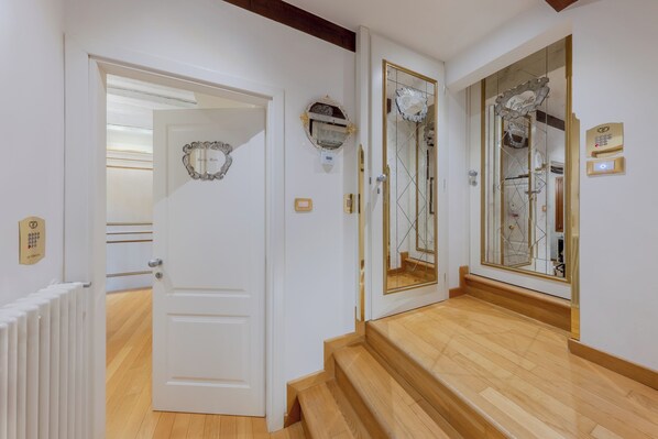 Un couloir avec une porte blanche, un miroir doté d’un cadre doré et une petite plaque fixée au mur.