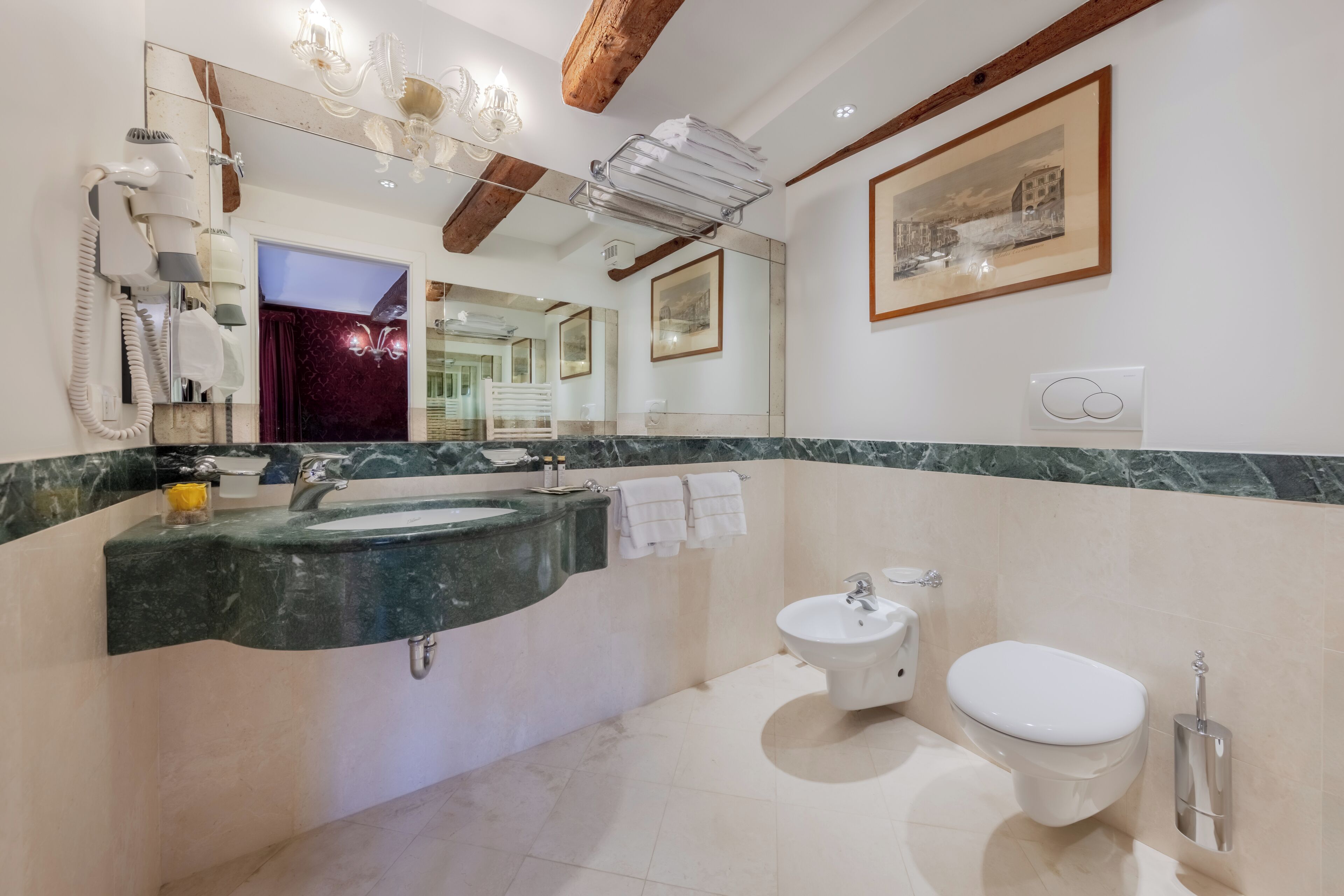 A modern bathroom with a marble sink, a bidet, and a toilet. There is a hairdryer on the wall, a towel rack, and a framed picture on the wall.