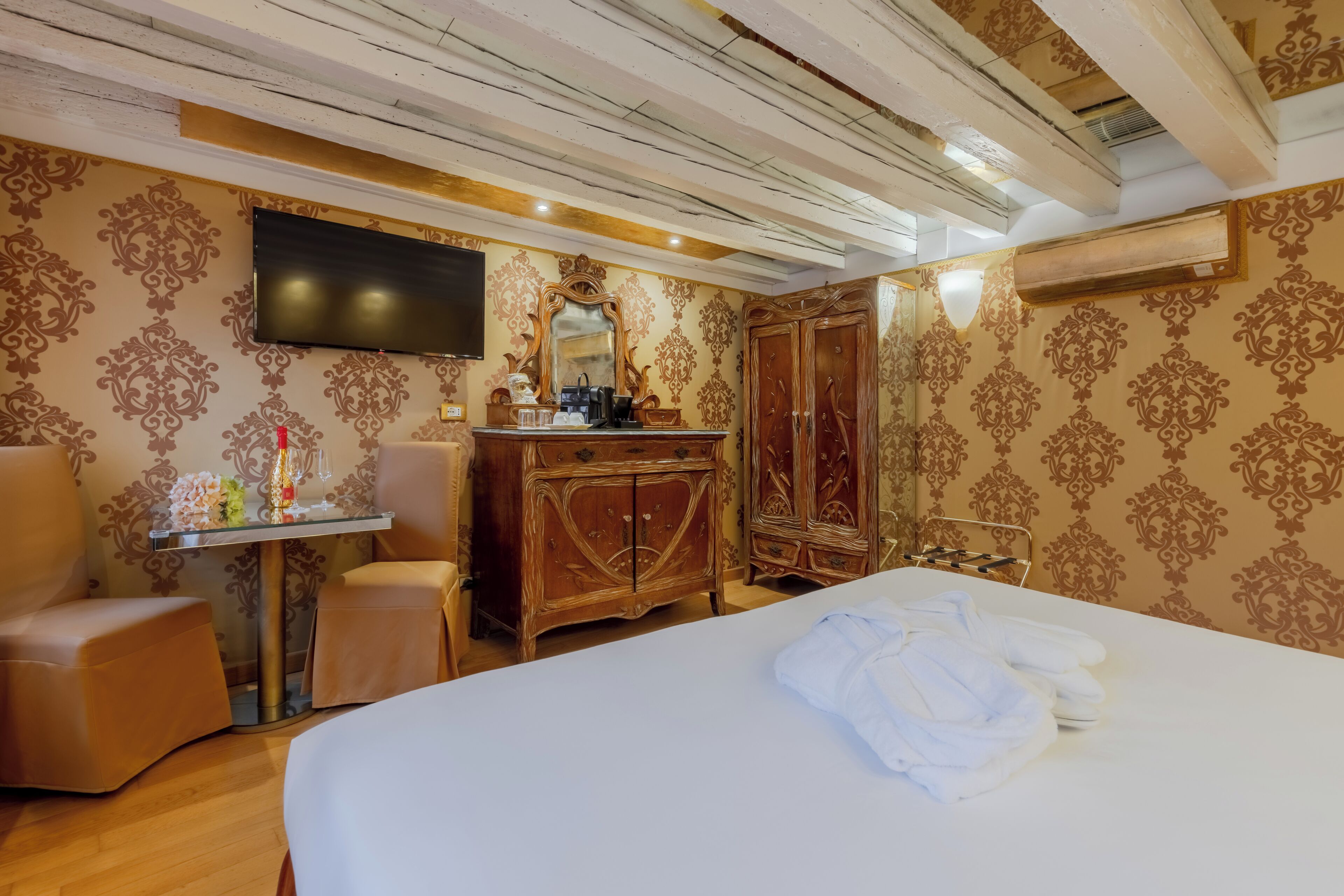 A hotel room with a large bed, a wooden dresser, a television, and a seating area with a chair and ottoman.