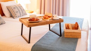 Una camera d'albergo con un letto, un comodino in legno con prodotti per la colazione, un cesto di vimini e una lampada a sospensione.