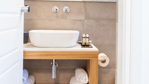 Un bagno moderno con lavandino bianco, mobile contenitore in legno e uno specchio sopra. Sul mobile ci sono asciugamani e articoli da toilette.