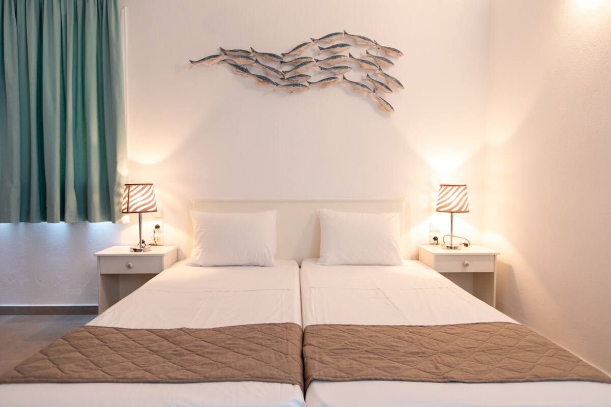 A double bed with a brown quilt, two bedside tables with lamps, and a wall art piece above the bed.