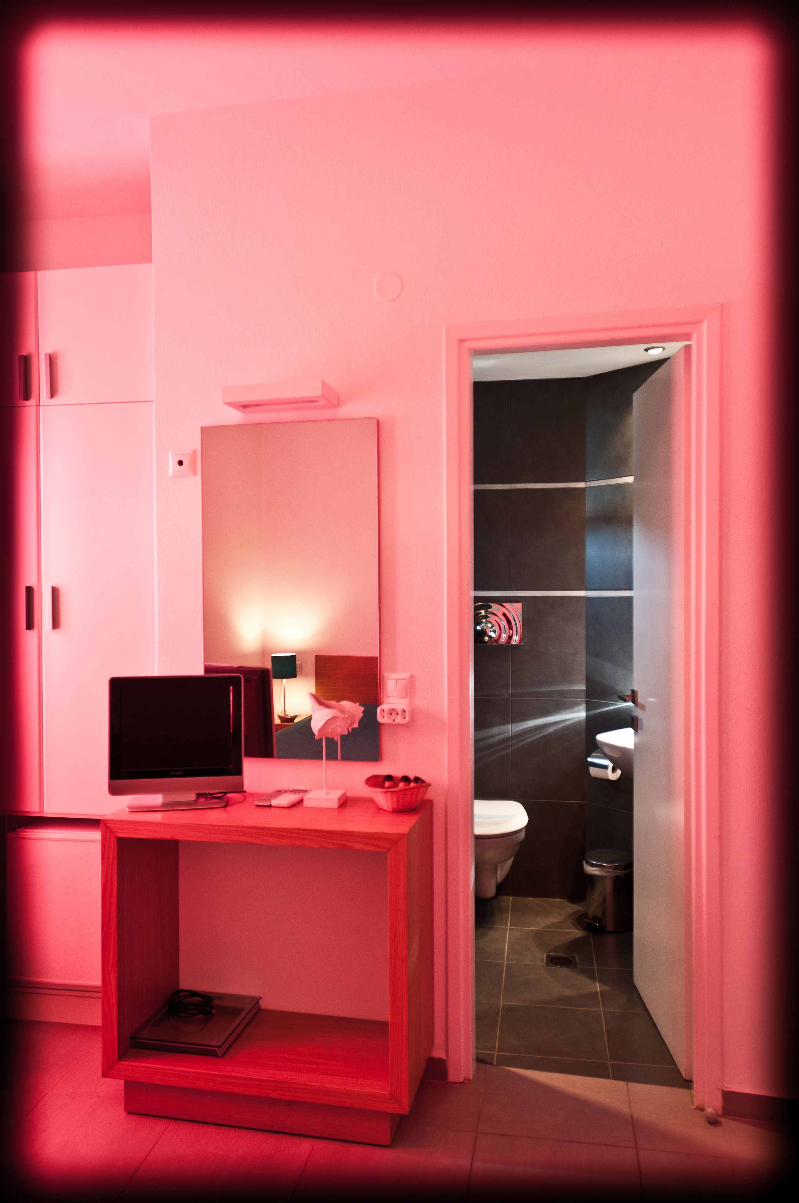 A modern bathroom with a pink theme, including a vanity with a mirror, a toilet, and a shower area.