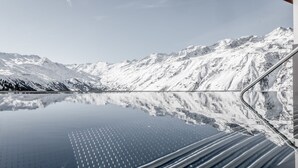 Una cordillera nevada reflejada en un lago tranquilo, con una carretera serpenteando entre las montañas.