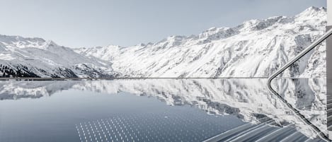 Una cordillera nevada reflejada en un lago tranquilo, con una carretera serpenteando entre las montañas.