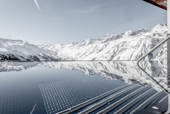 A snow-covered mountain range reflected in a calm lake, with a road winding through the mountains.