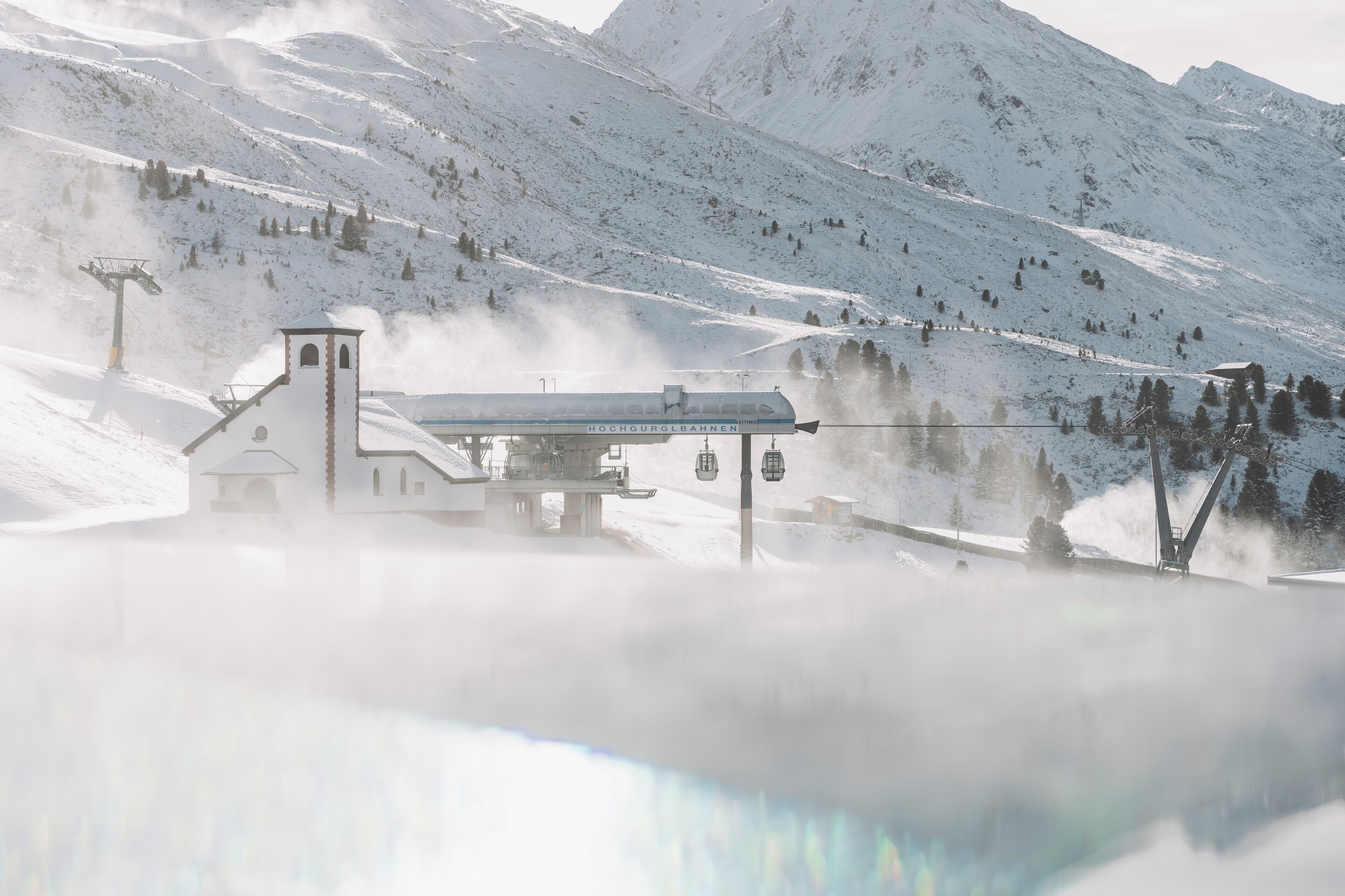 A snow-covered mountain with a ski lift and a building with a sign reading "HOCHGURGLBAHENEN".