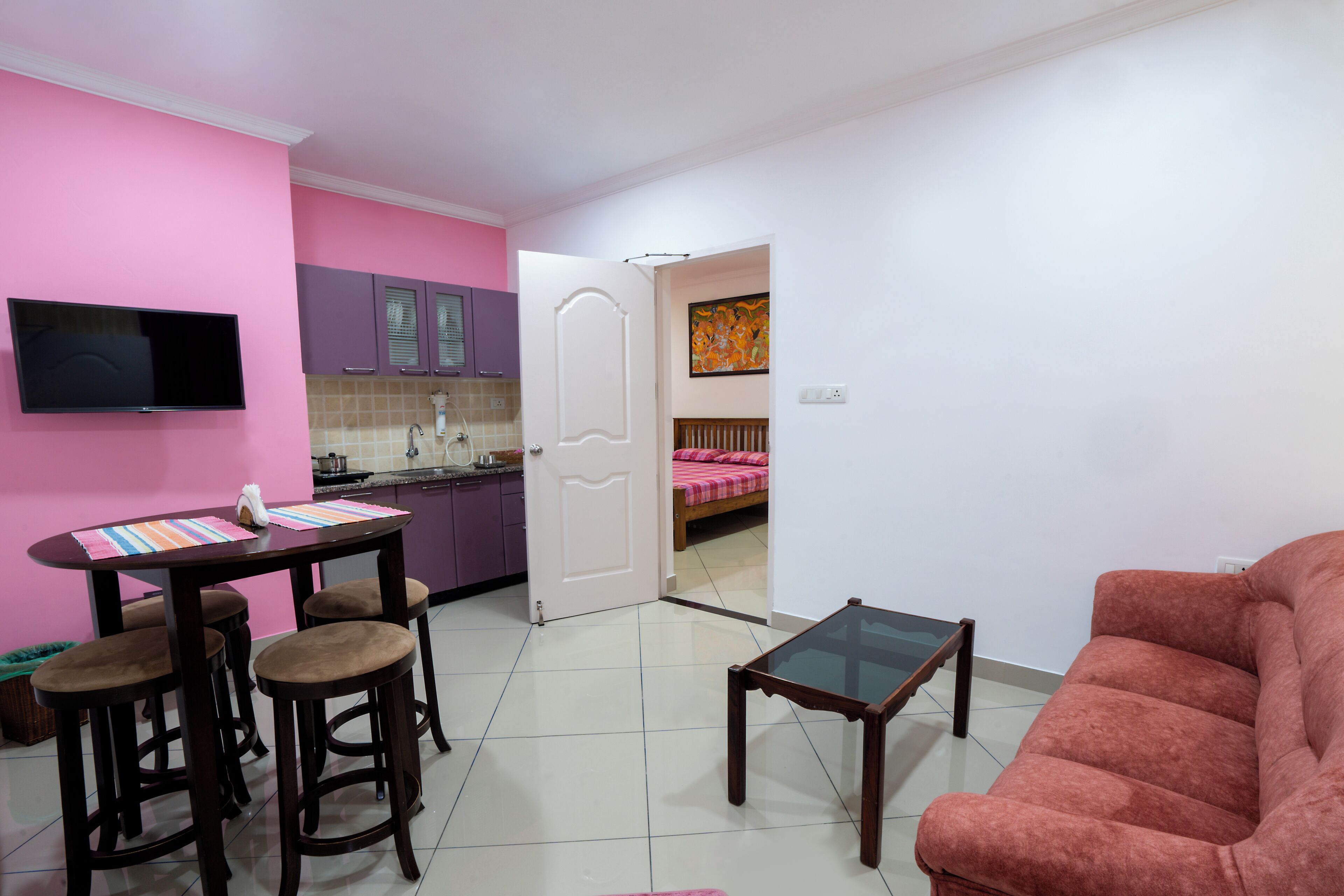 Un espacio habitable compacto con comedor, sofá, televisor y cocina al fondo.
