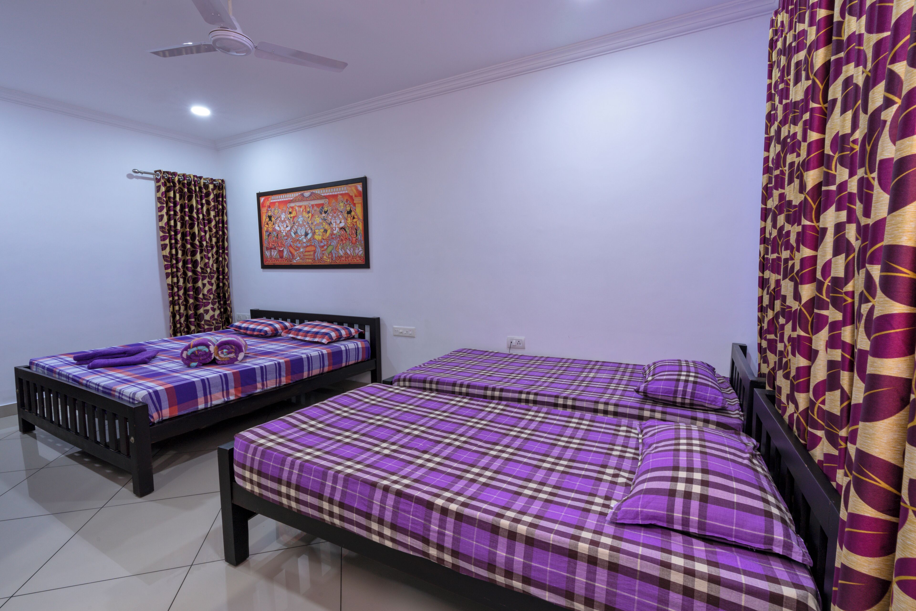 A bedroom with two beds, a ceiling fan, and a wall-mounted painting.