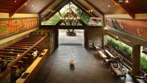 A spacious lobby with a high ceiling, wooden beams, a chandelier, and a large mural on the walls. - Uday Suites (Thiruvananthapuram)