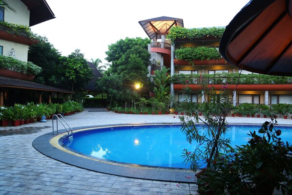 A swimming pool surrounded by potted plants and a building with balconies.