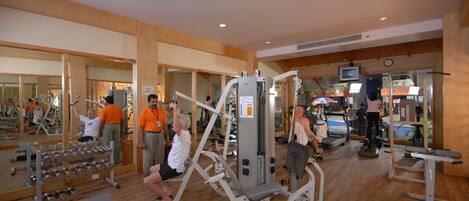 Un gimnasio con diversos equipos de ejercicio, suelos de madera y espejos en las paredes.