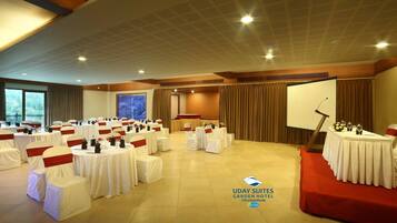 Un salón de conferencias con varias mesas y sillas, un atril y una pantalla de proyección.
