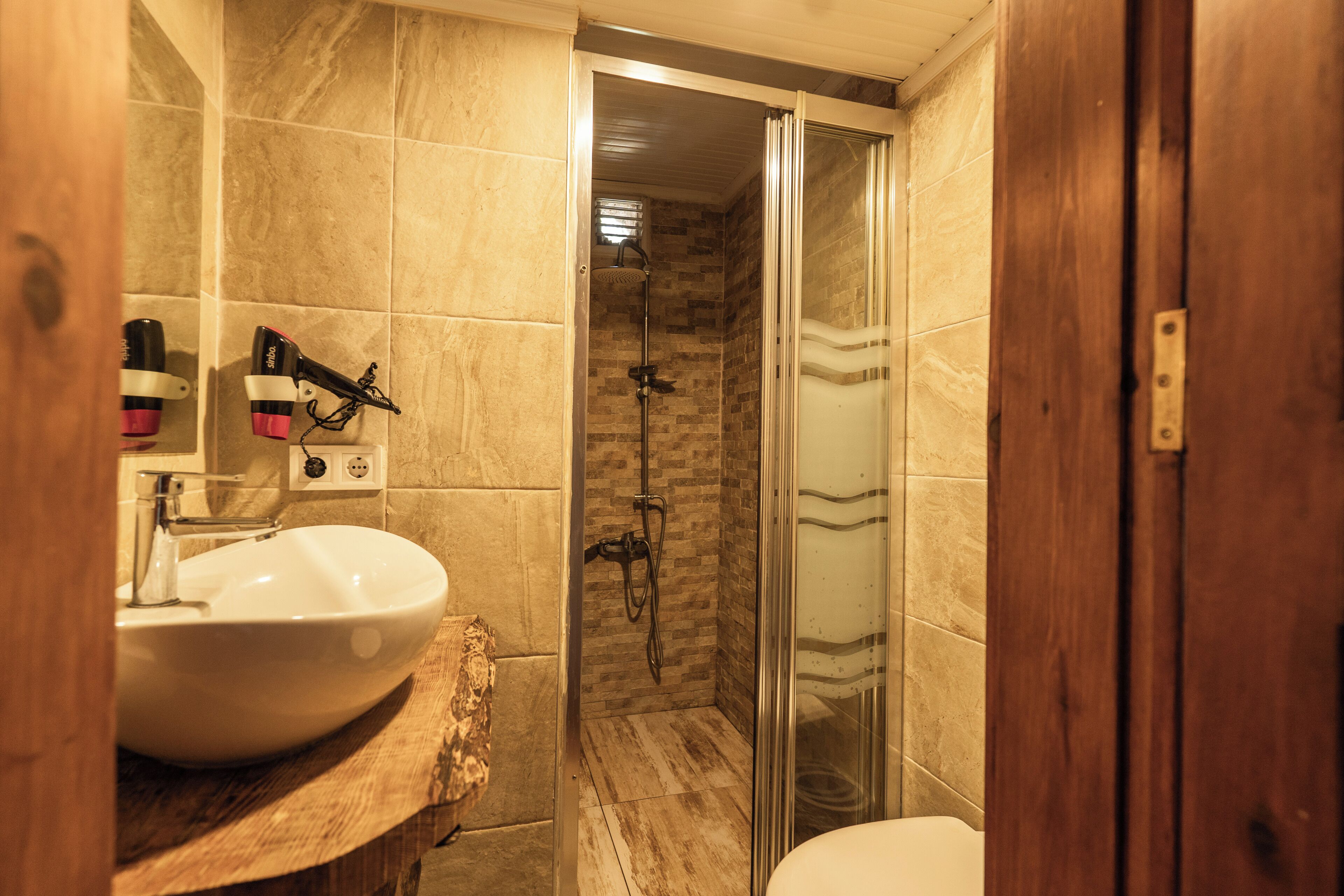 Un baño con lavamanos blanco, cabina de ducha de cristal y tocador de madera.