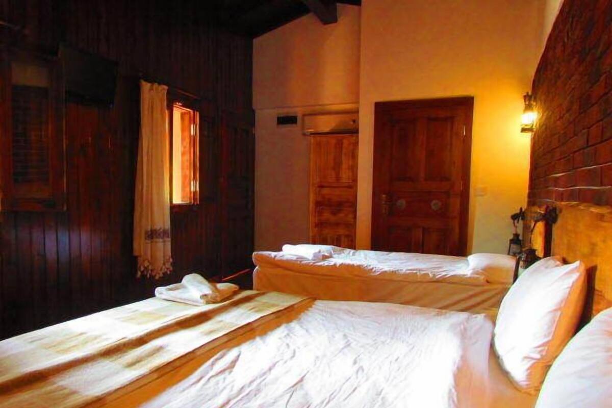 Una habitación con dos camas, paredes y puerta de madera, y una lámpara fijada a la pared.