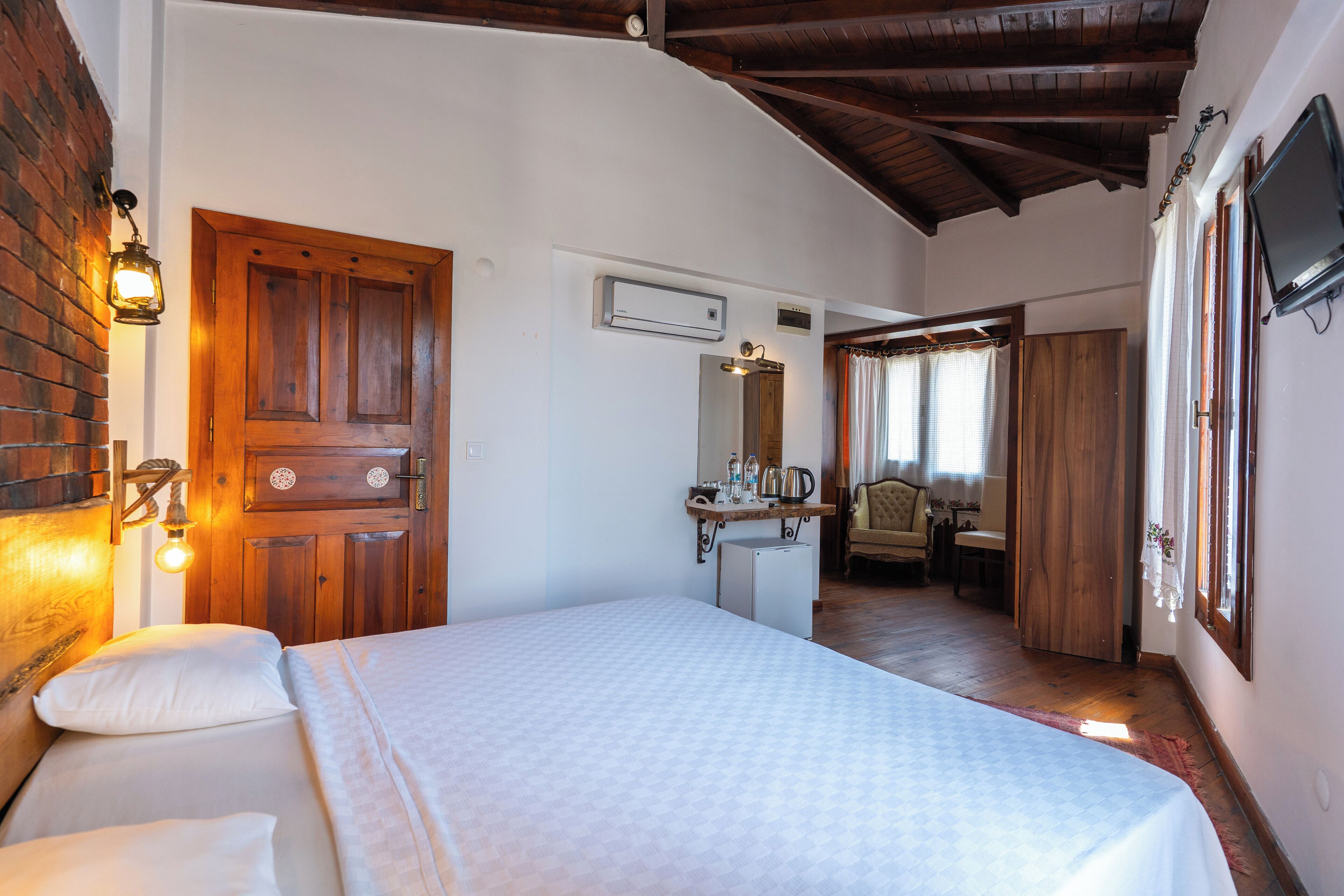 Un dormitorio con cama, una puerta de madera, un escritorio pequeño con silla y un televisor en la pared.
