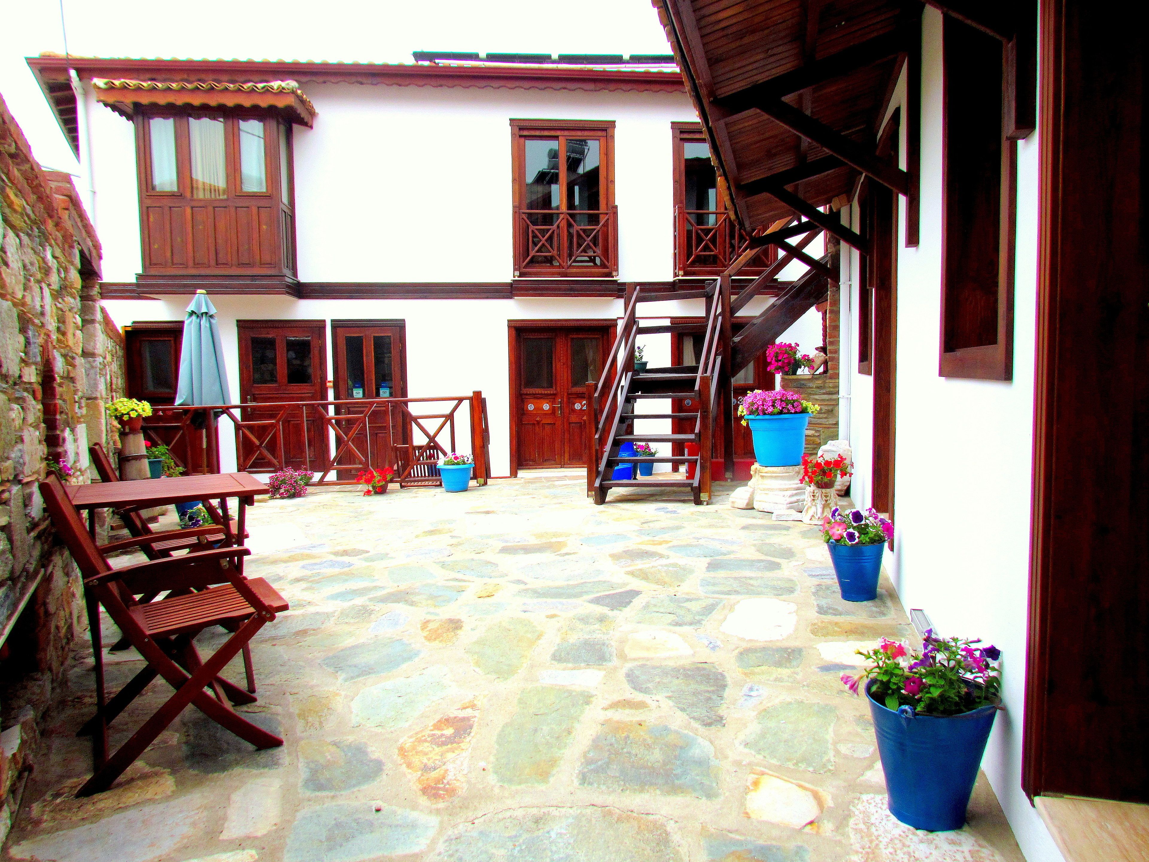 A courtyard with stone flooring, wooden furniture, and potted plants.