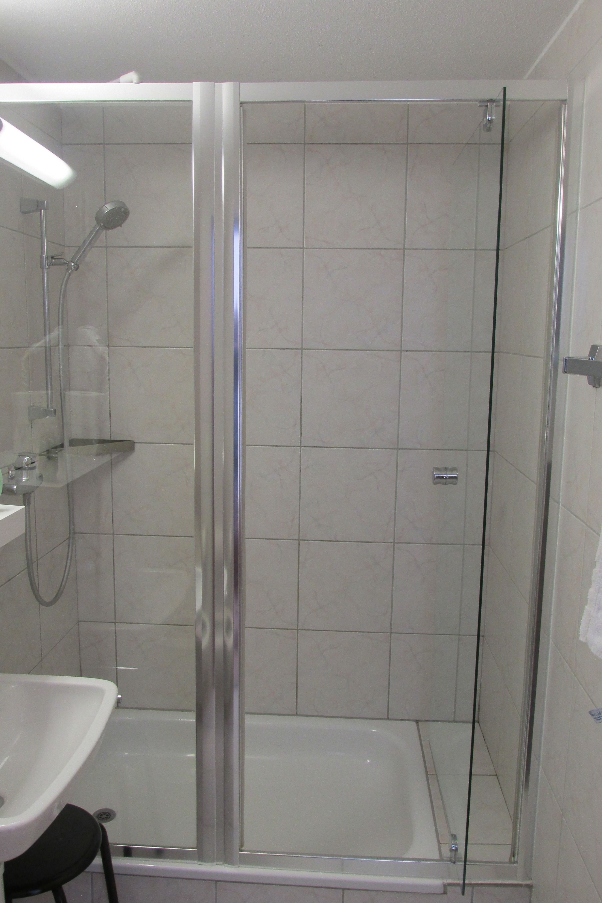 A glass-enclosed shower stall with a white bathtub and a visible showerhead.