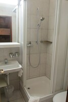Un pequeño espacio de ducha cerrado, con un lavamanos blanco y un espejo encima.