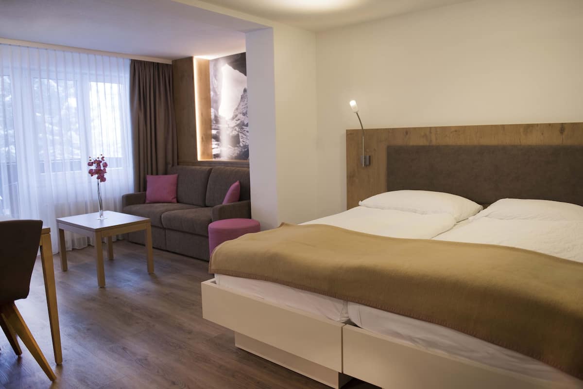 A modern hotel room with a large bed, a sofa, a small table, and a chair.