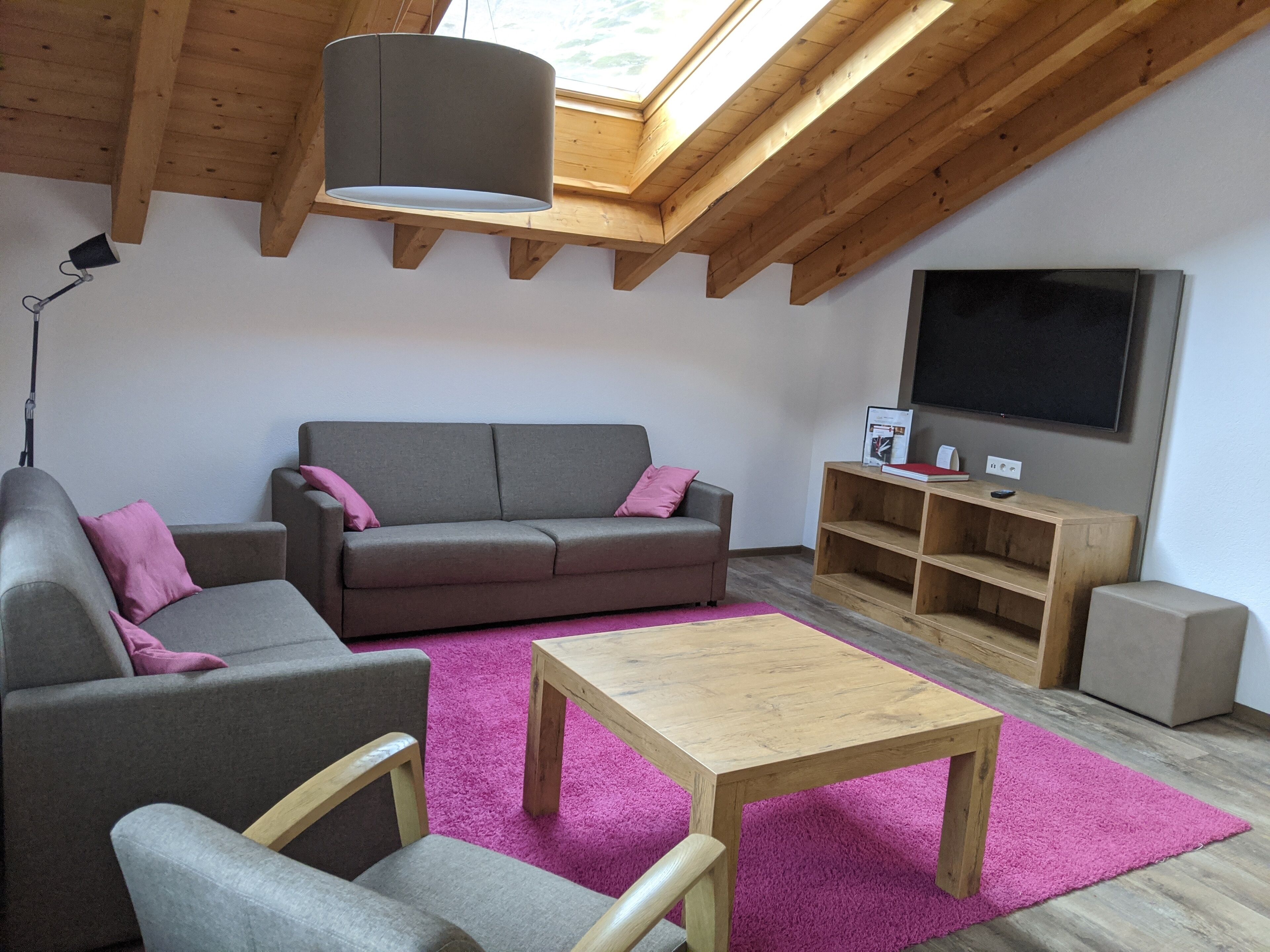 Un salón estilo loft con un sofá gris, una mesa de centro de madera y una alfombra rosa.