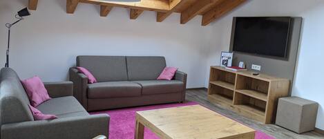 Un salón estilo loft con un sofá gris, una mesa de centro de madera y una alfombra rosa.