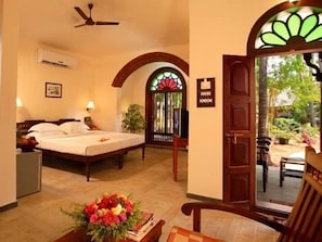 A hotel room with a bed, a desk, a chair, a flower arrangement, and a view of the outside. - Cherai Beach Resort (Kochi)