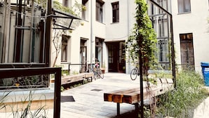 Un patio con un banco de madera, bicicletas y un cubo de basura azul.