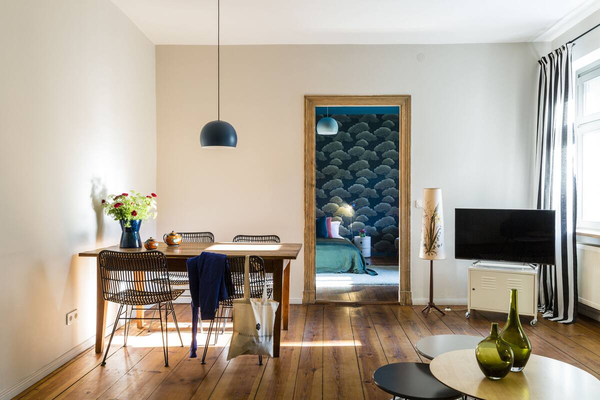 A modern living room with a dining area, wooden flooring, a TV, and a wall with a cloud pattern.