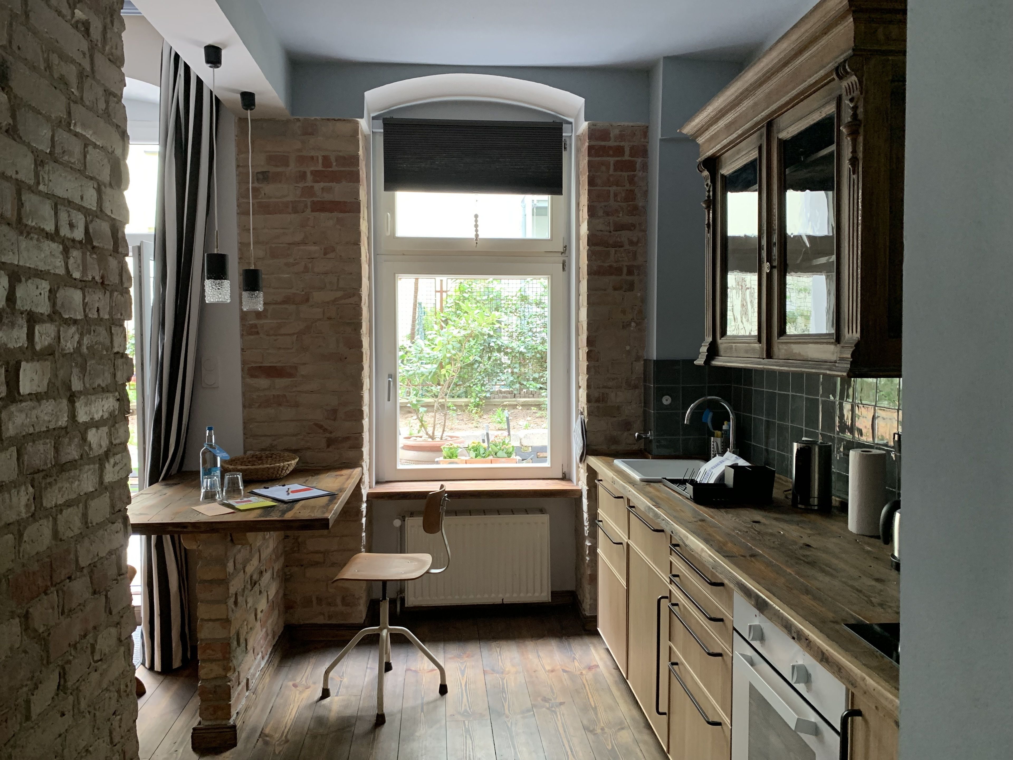A kitchen with a large window, wooden cabinets, a radiator, and a small table with a chair.